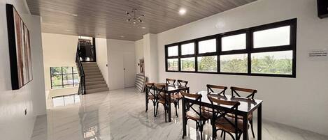 A spacious room with a polished marble floor, a staircase leading to another level, and a large window with a view of greenery.