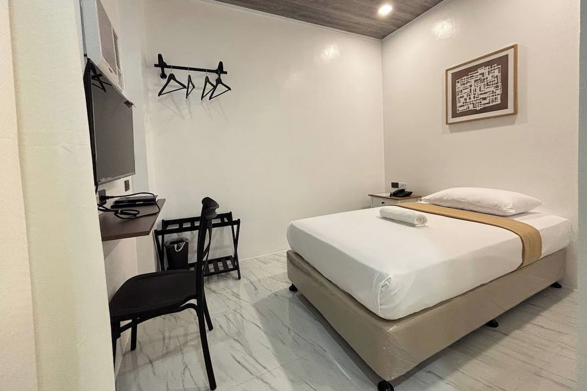 Ein modernes Hotelzimmer mit Bett, Schreibtisch mit Stuhl, Fernseher und Kleiderhaken.