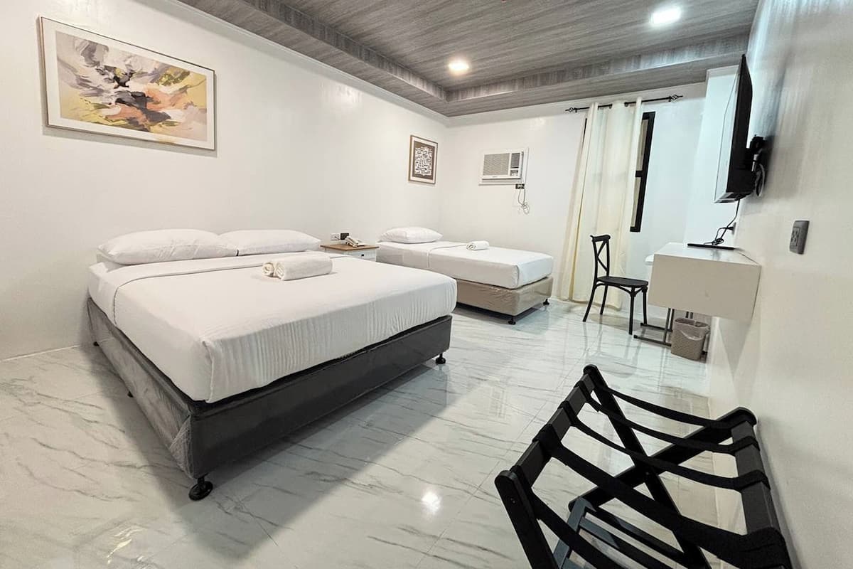 Ein Hotelzimmer mit einem großen Bett, einem Einzelbett, einem Schreibtisch mit Stuhl, einem Fernseher und Bildern an den Wänden.