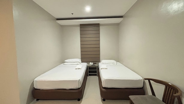 A small, clean room with two single beds, a nightstand, a chair, and a wooden slat wall. - Hotel De Alexa (Maramag)