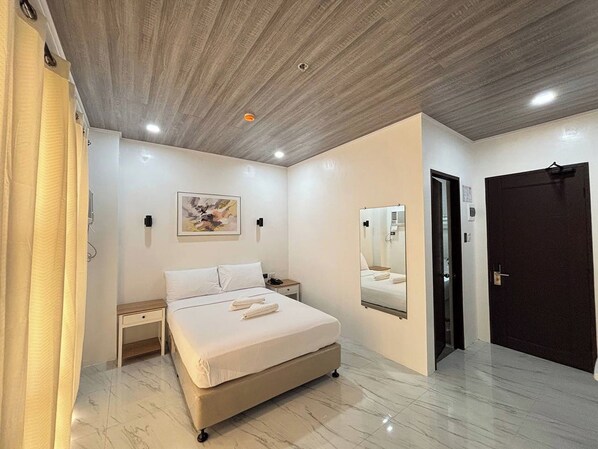 A modern bedroom with a bed, bedside tables, a mirror, and a door. - Hotel De Alexa (Maramag)