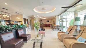 A modern hotel lobby with leather sofas, a glass coffee table, and a dining area with tables and chairs. - Hotel De Alexa (Maramag)