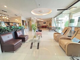 A modern hotel lobby with leather sofas, a glass coffee table, and a dining area with tables and chairs.