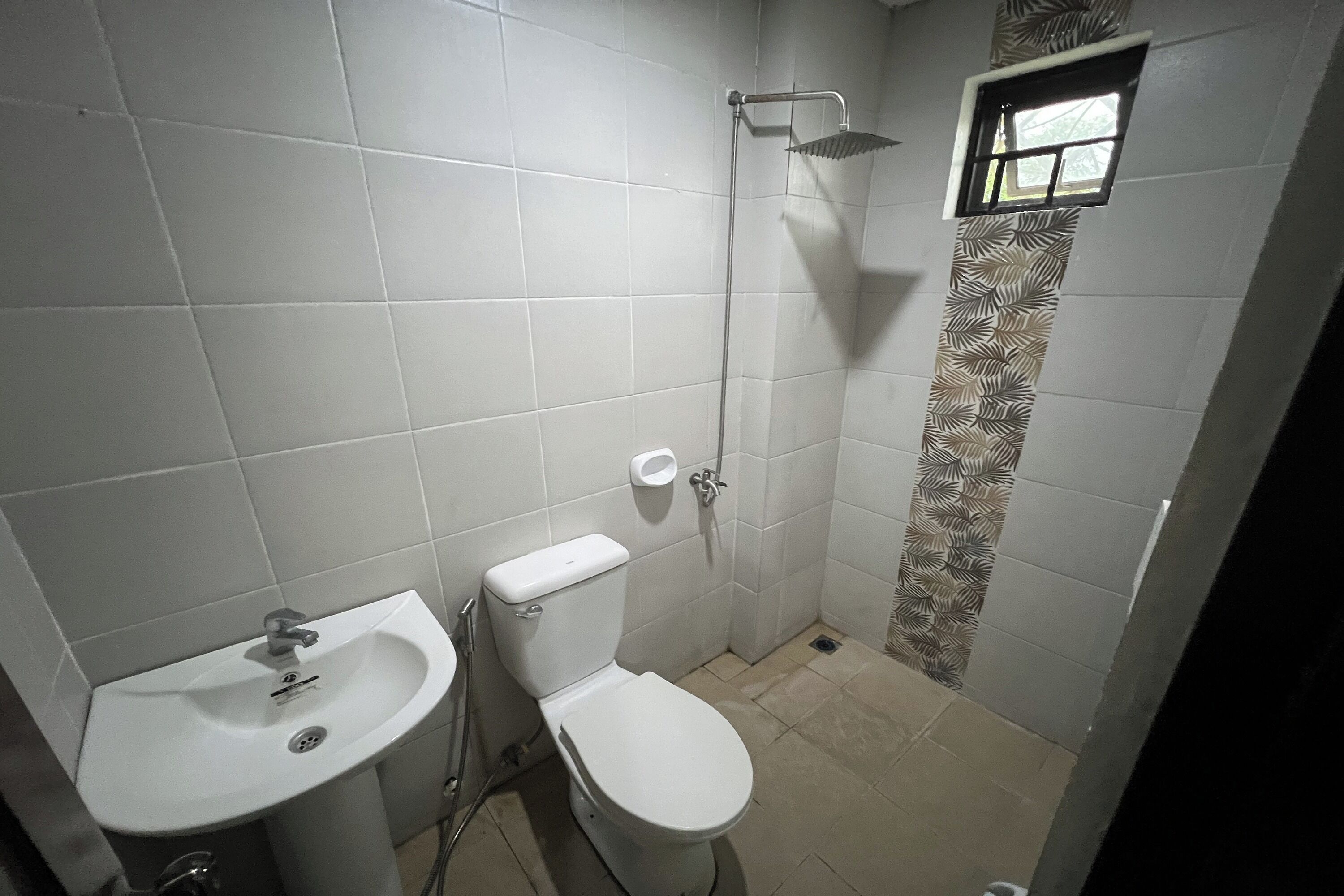 A bathroom with a sink, toilet, shower, and a small window.