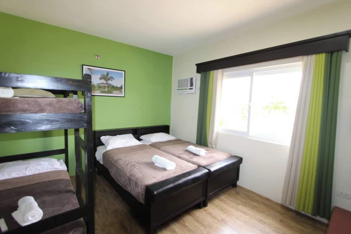 A hotel room with a bunk bed, a single bed, and a window with curtains.