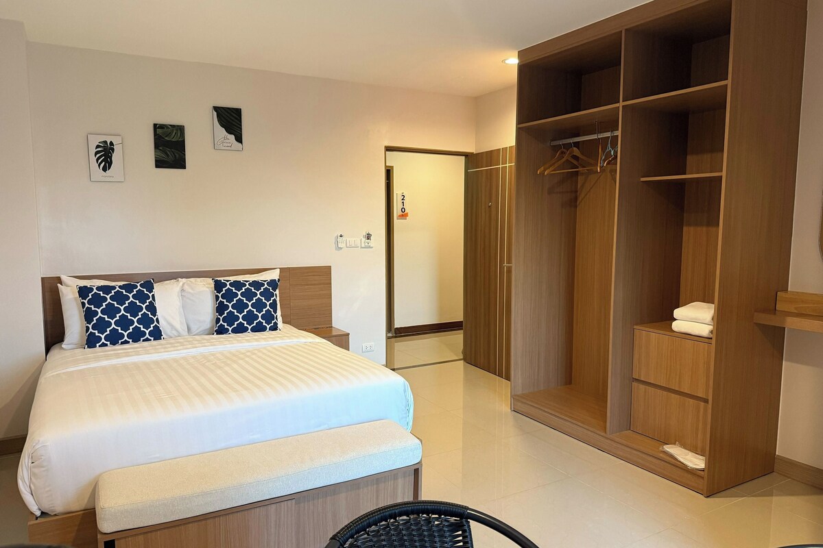 A hotel room with a bed, a wooden wardrobe, a bench, and a chair.