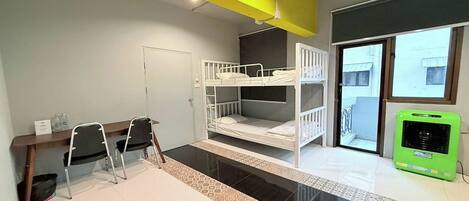 A room with bunk beds, a desk with chairs, a trash bin, and a window with a view.