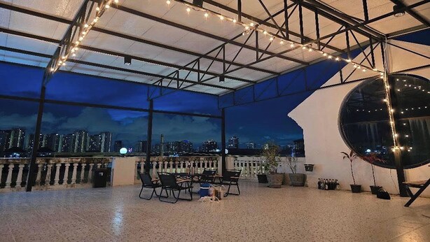 A rooftop terrace with a city view, string lights, and outdoor seating.