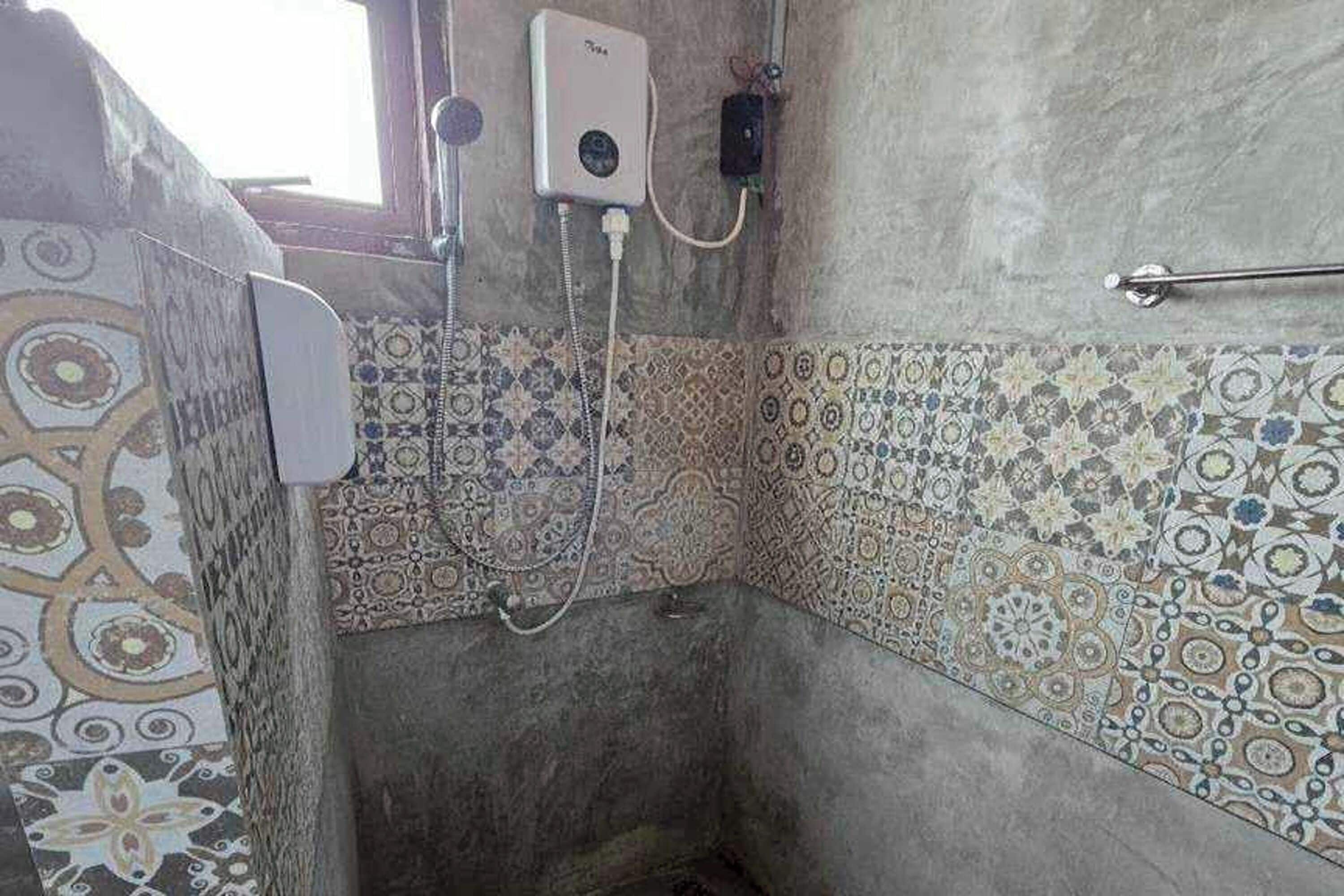A bathroom with patterned tiles, a handheld showerhead, and a towel rack.
