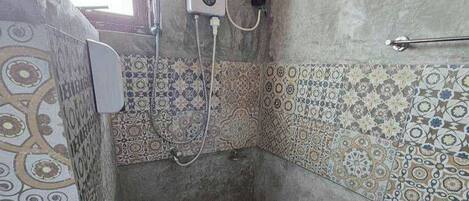 A bathroom with patterned tiles, a handheld showerhead, and a towel rack.