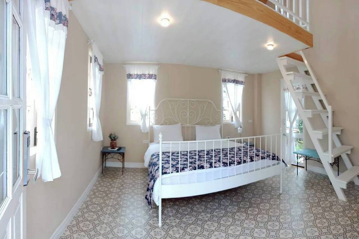 Ein Schlafzimmer mit Bett, Fenster, Treppe und einem kleinen Tisch mit Pflanze.