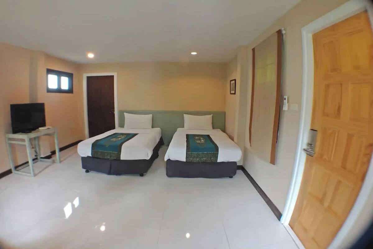 Ein Hotelzimmer mit zwei Betten, einem Fernseher auf einem kleinen Tisch und einer Holztür.