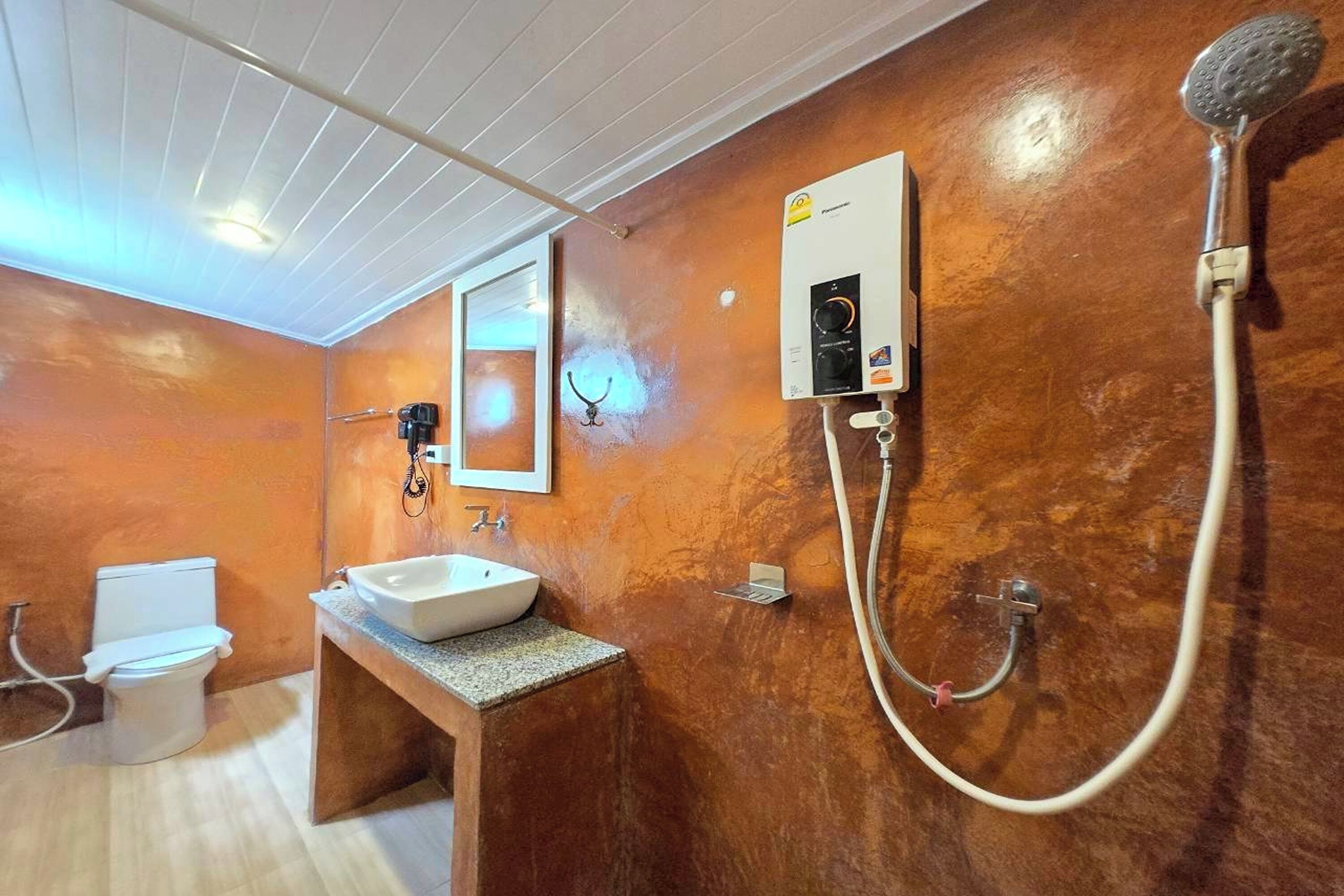 A bathroom with a white toilet, a sink, a shower with a handheld showerhead, and a towel rack.