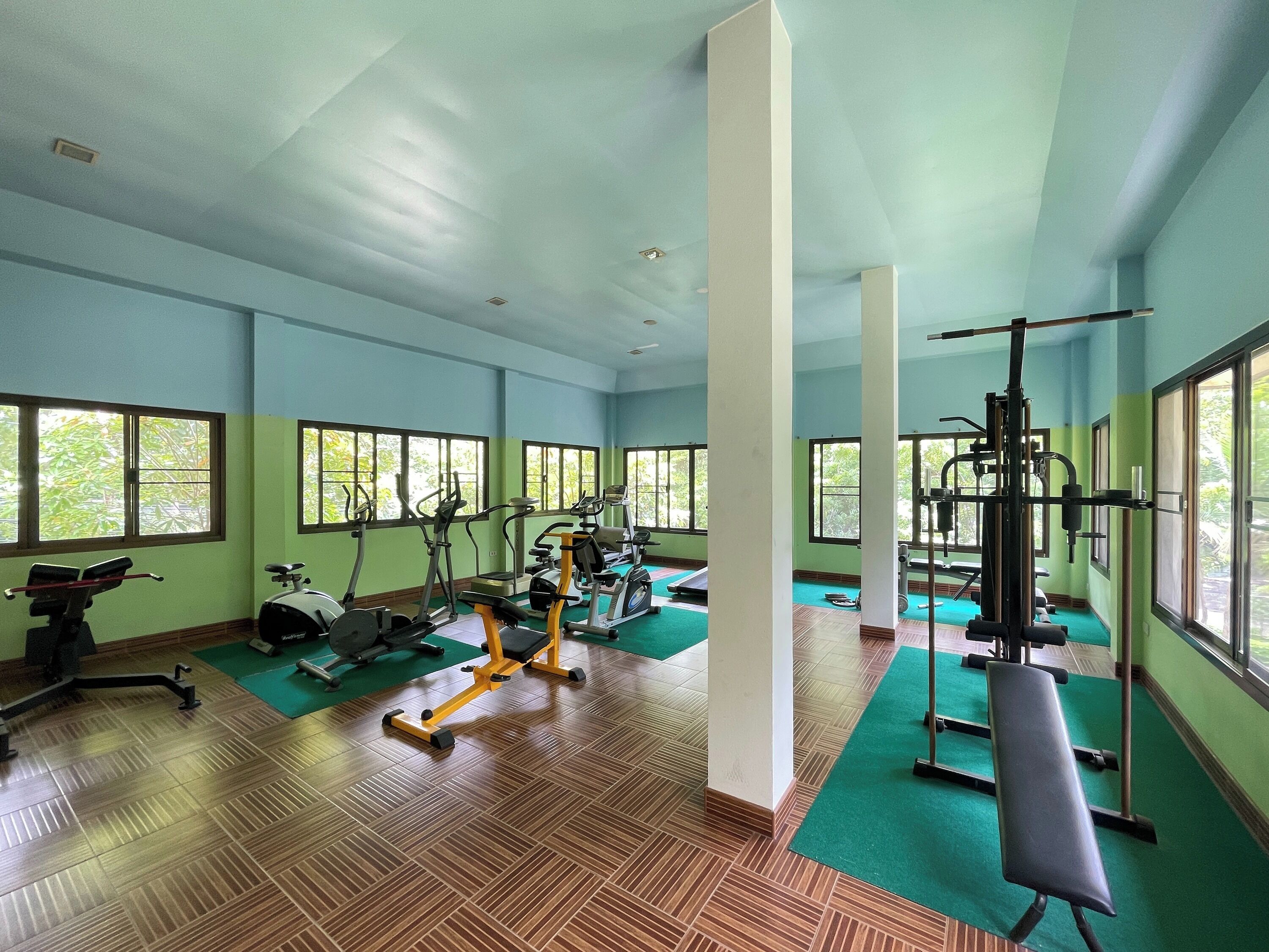 Un gimnasio con equipo de ejercicio, ventanas amplias y piso de madera.
