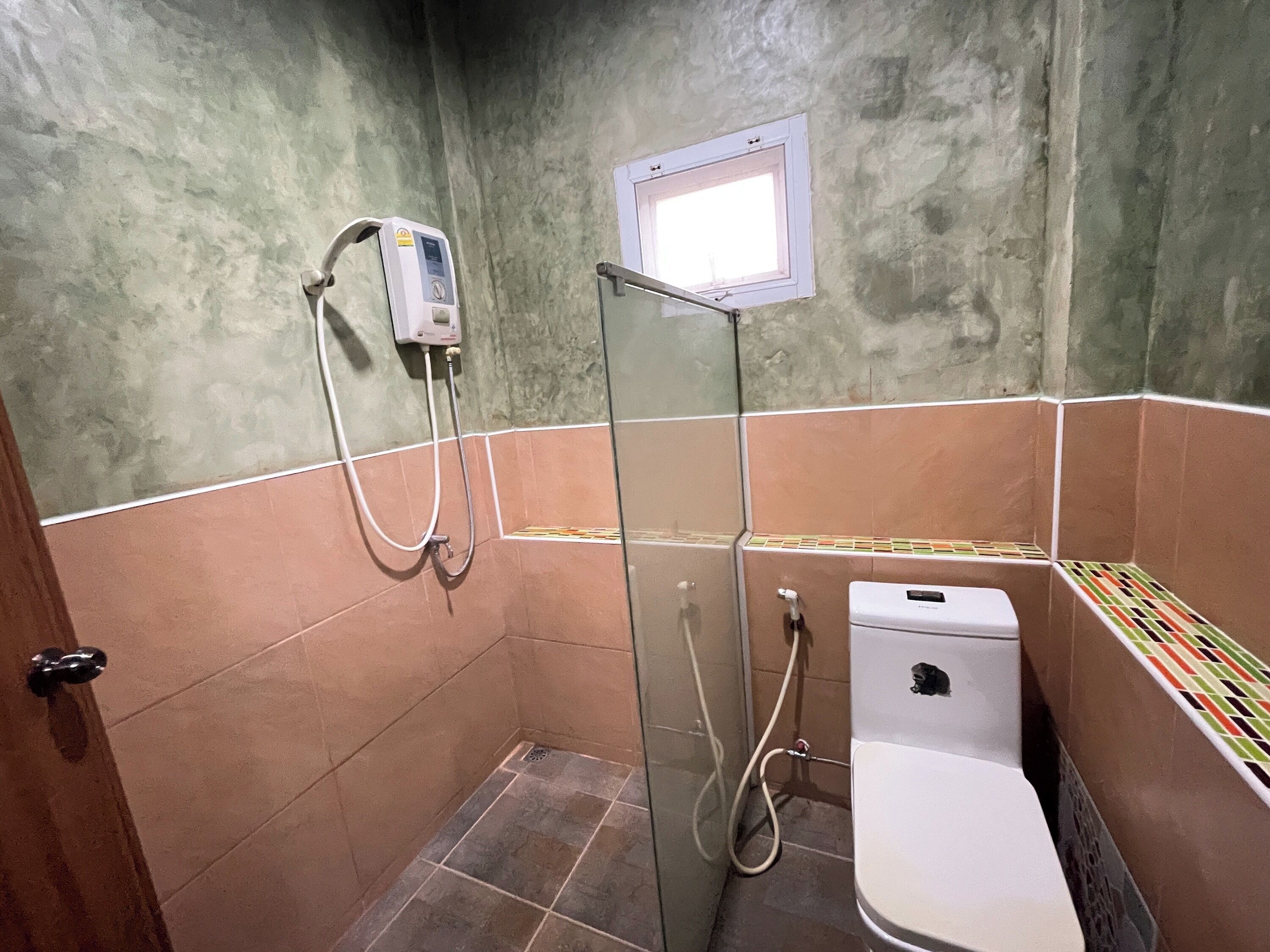 A small bathroom with a shower, toilet, and a window.