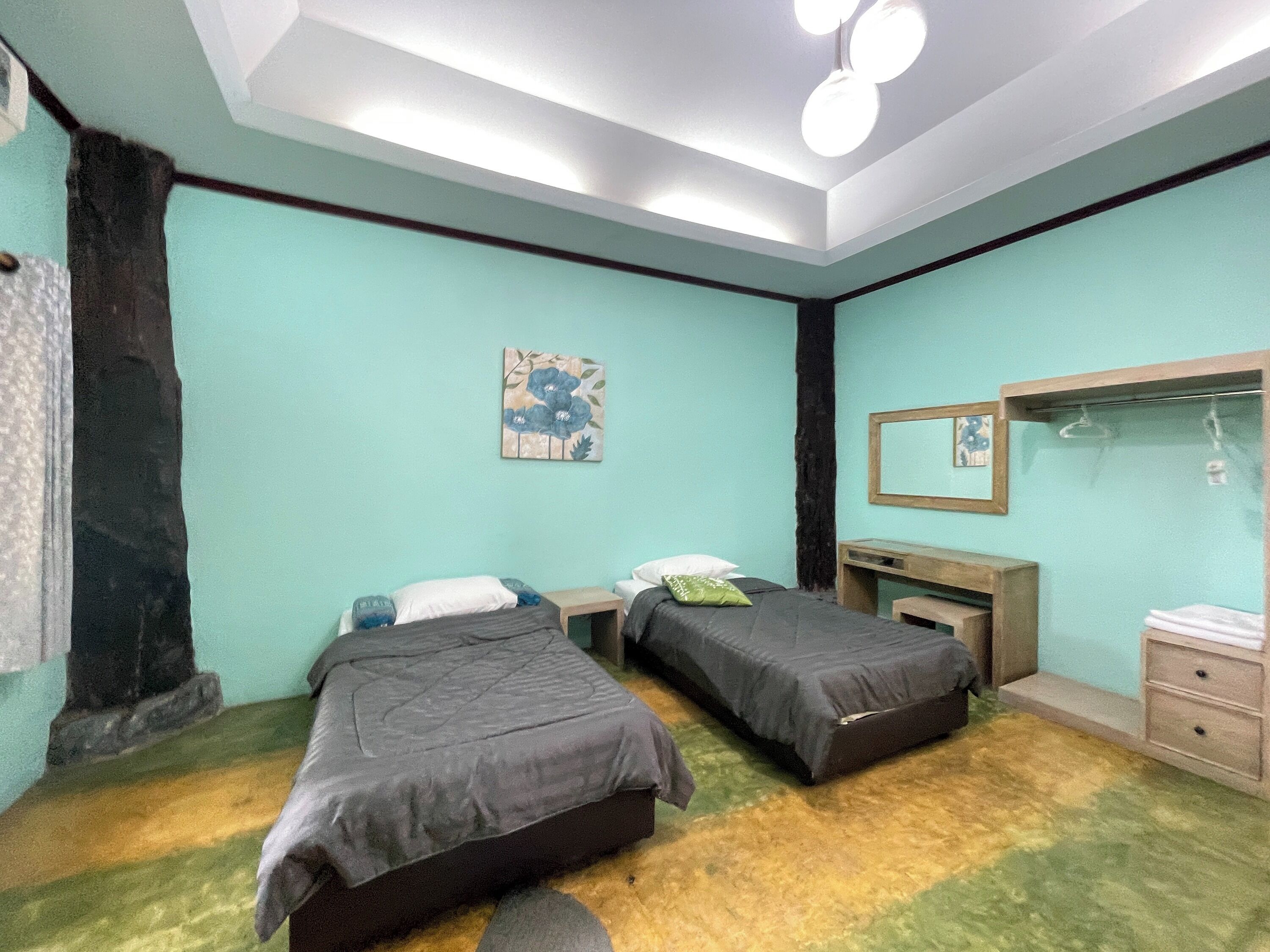 A bedroom with two beds, a desk, a mirror, and a wall-mounted artwork.