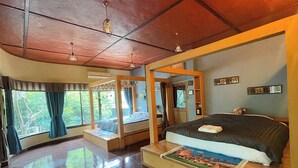 Ein Schlafzimmer mit einem großen Bett, einem kleineren Bett und einer Sitzecke mit Blick auf Bäume.