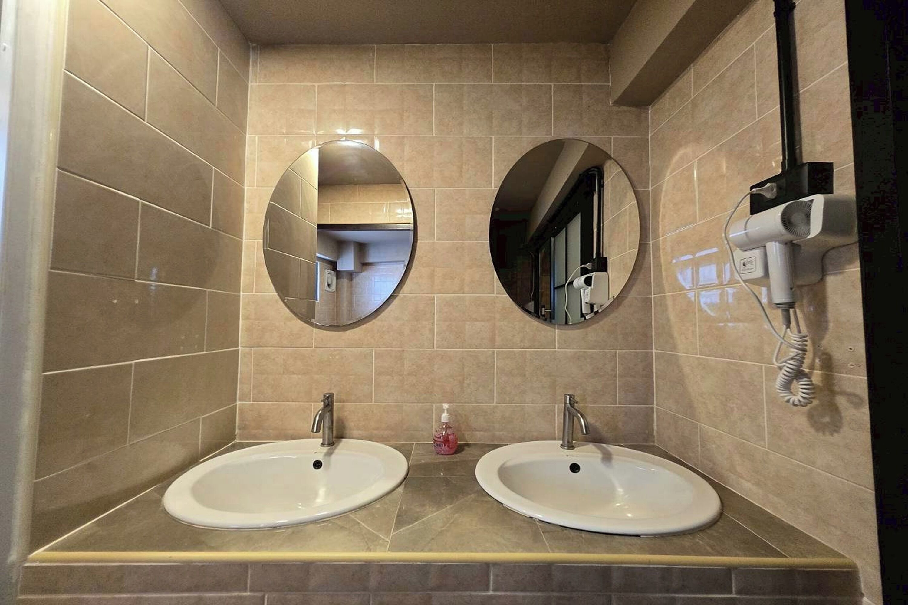 A bathroom with two sinks, two mirrors, and a hairdryer on the wall.