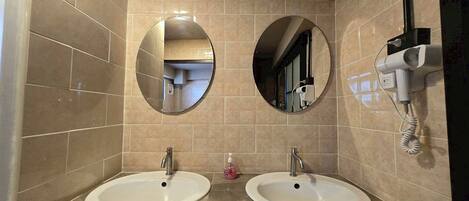A bathroom with two sinks, two mirrors, and a hairdryer on the wall.