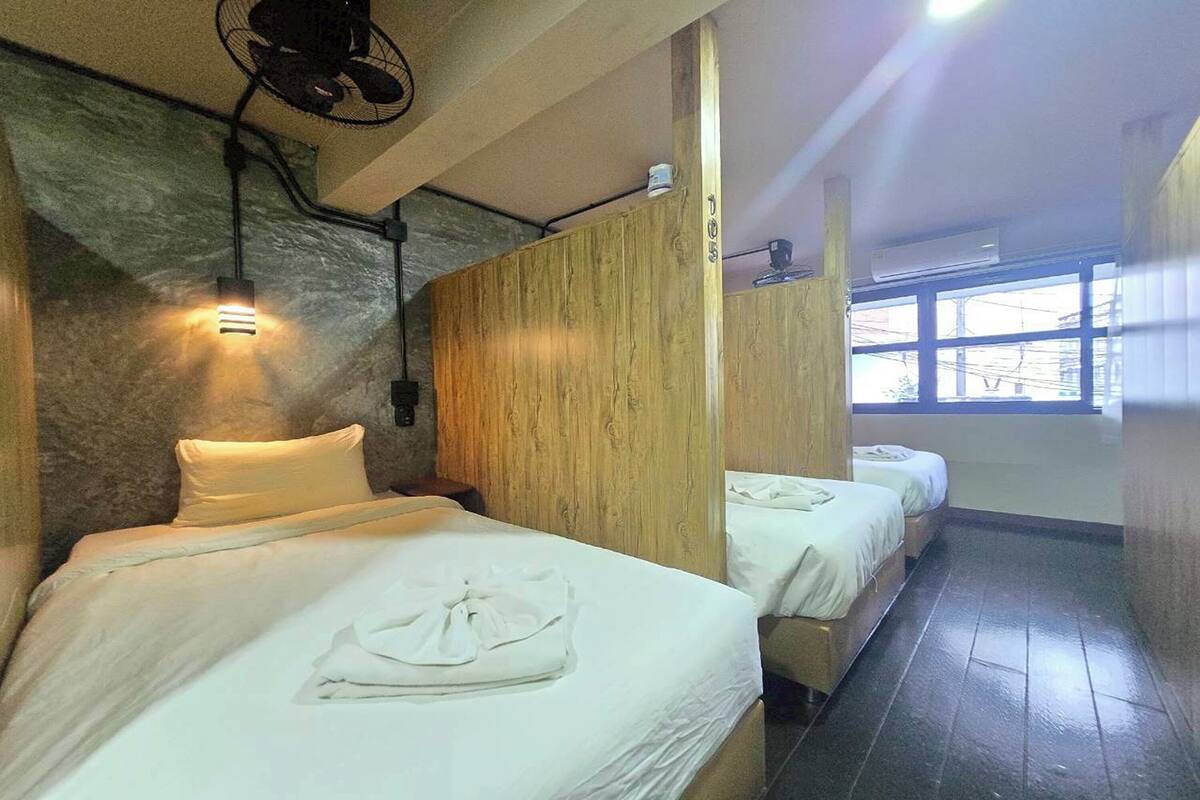 A hotel room with two beds, a stone wall, wooden paneling, a fan, and an air conditioning unit.
