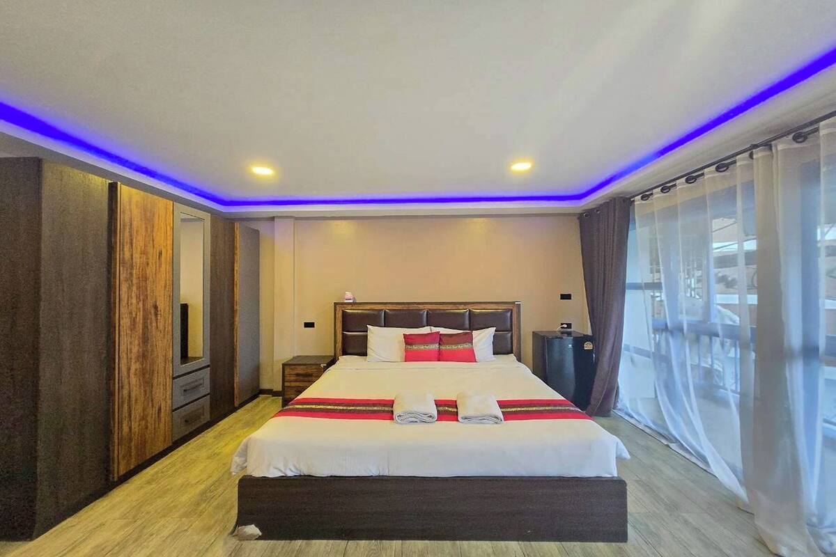 A modern hotel room with a large bed, wooden paneling, a nightstand, and a view of the outdoors.
