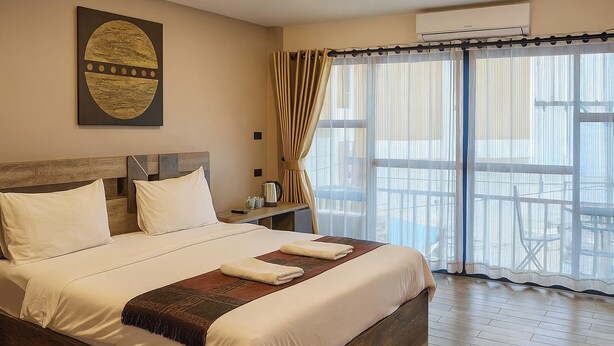 A neatly made bed with white linens and a brown throw blanket, a wooden headboard, and a large window with sheer curtains. - Central Guesthouse Chiang Rai (Chiang Rai)