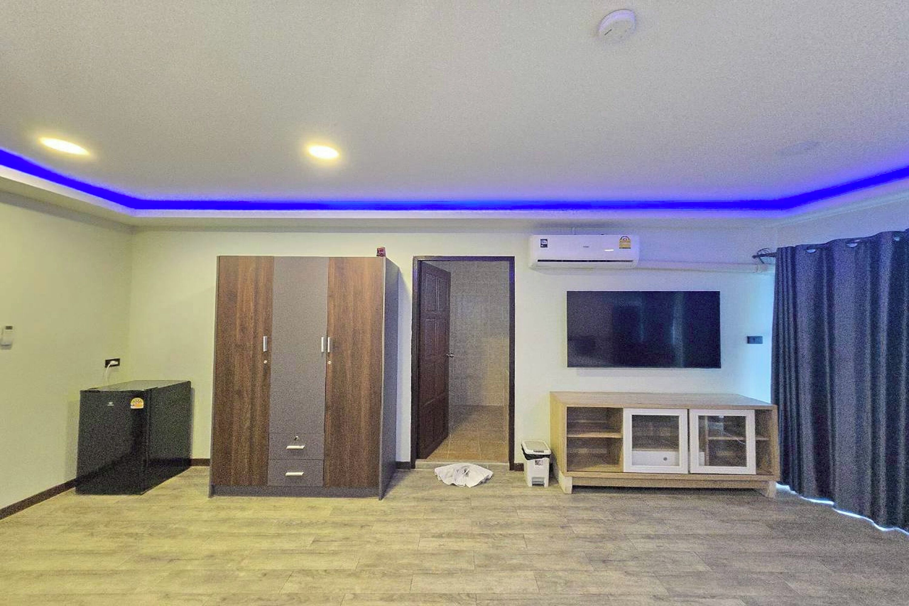 A modern living room with a wooden wardrobe, a TV mounted on the wall, and a small cabinet.