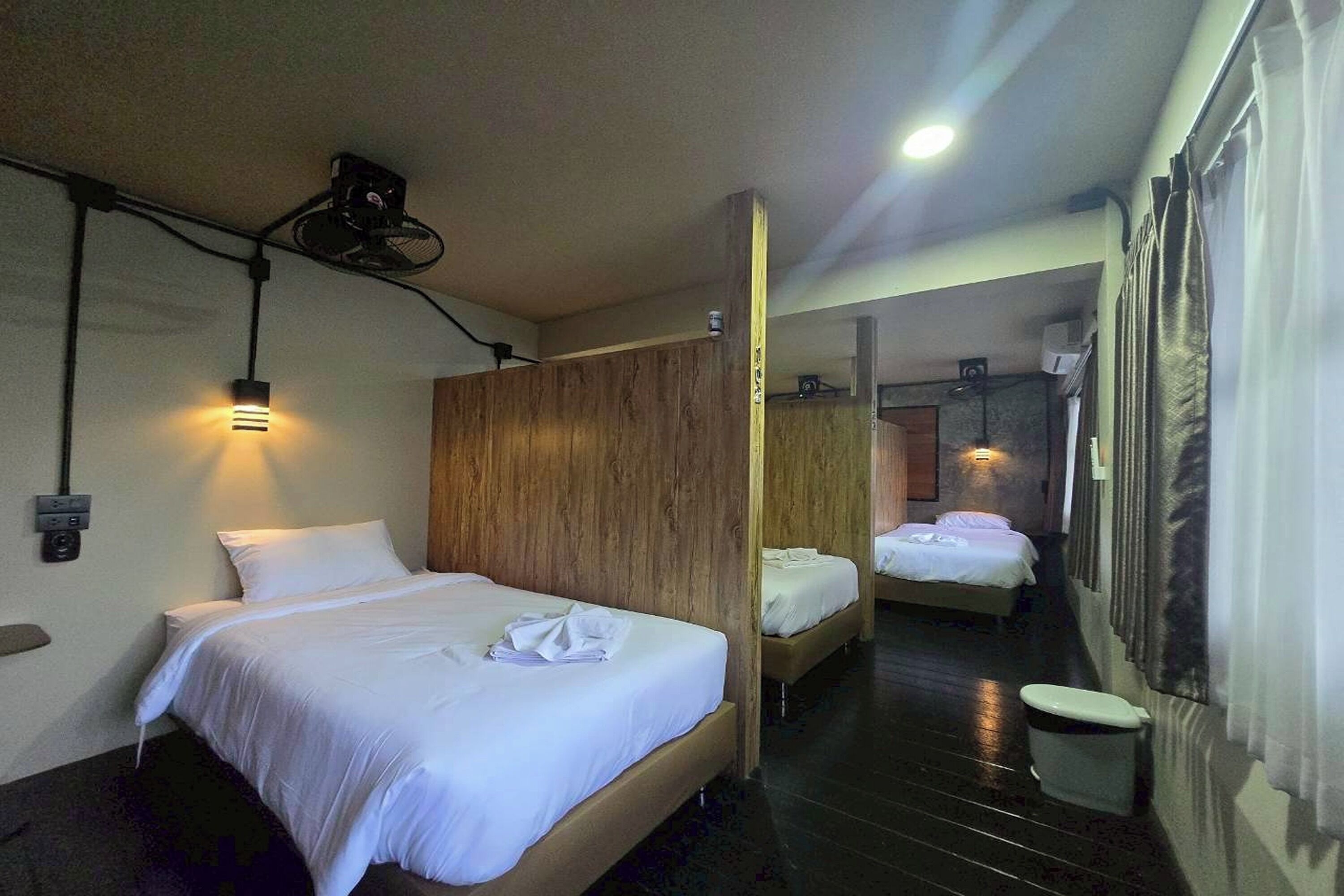 A hotel room with a wooden partition, a bed with white linens, a small bedside table, a wall-mounted projector, and a ceiling light.