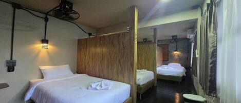 A hotel room with a wooden partition, a bed with white linens, a small bedside table, a wall-mounted projector, and a ceiling light.