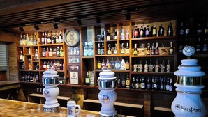 A bar with shelves of various liquor bottles, two large beer dispensers, and a clock on the wall. - Central Guesthouse Chiang Rai (Chiang Rai)