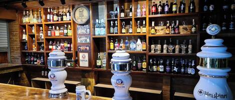 A bar with shelves of various liquor bottles, two large beer dispensers, and a clock on the wall.
