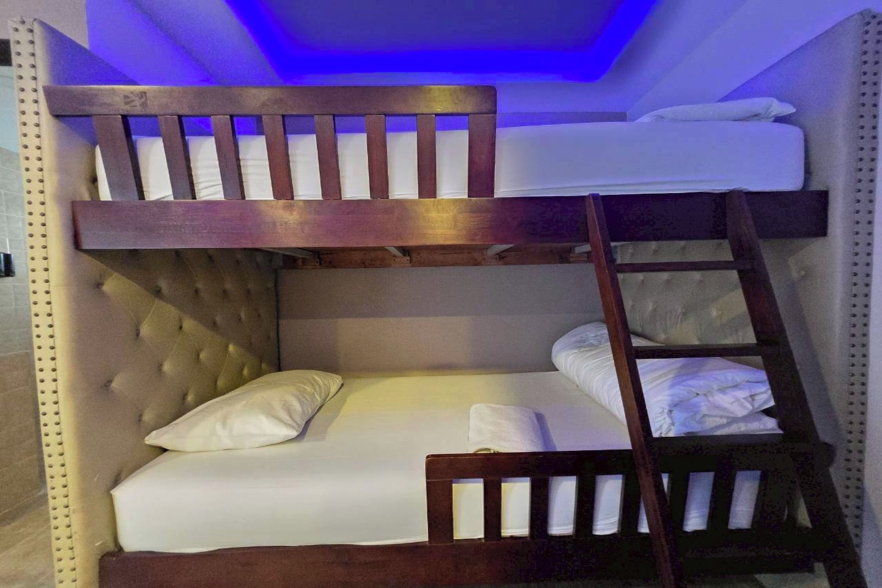 Una cama litera con escalera, cabecera tapizada y ropa de cama blanca.