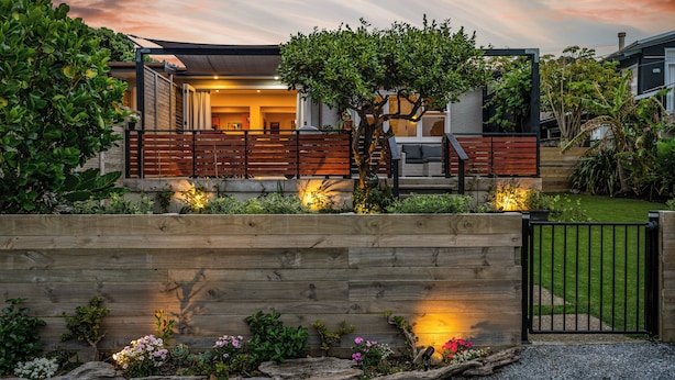 A modern house with a wooden deck, a tree, and a well-maintained garden.