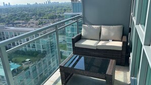 Varanda com sofá de vime e mesa de centro de vidro, com vista para a cidade.