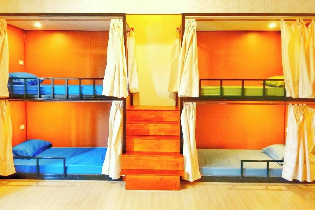 Una habitación con dos literas, cada una con cortina, y una escalera de madera en el centro.