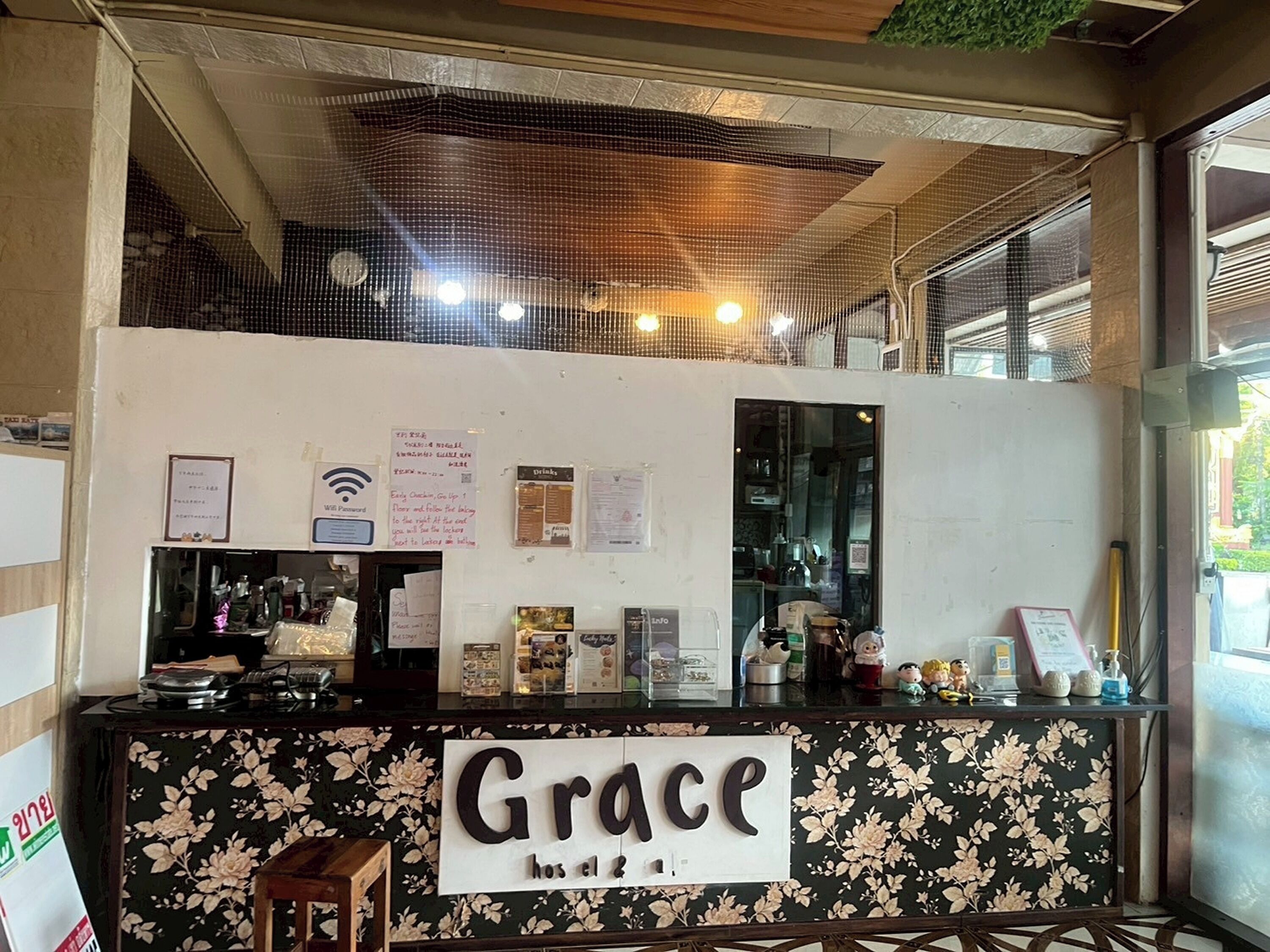 A cafe counter with a floral design and a sign that reads "Grace." There are various items on the counter, including a cash register, a menu board, and some decorative objects.
