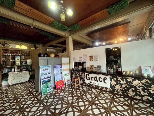 A reception area with a sign reading "Grace" and a patterned floor. There are informational posters and a counter with various items.