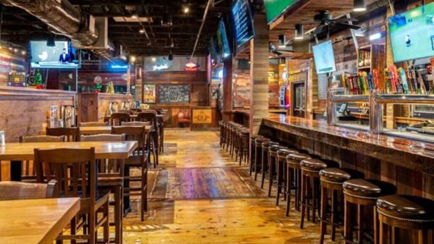 A bar area with wooden flooring, bar stools, and multiple screens displaying content.