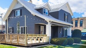 A two-story house with a covered porch, a small deck, and a well-maintained lawn. - Downtown Algoma - Walk to Beach, Shops, Marina. Easy access to Door County! (Algoma)