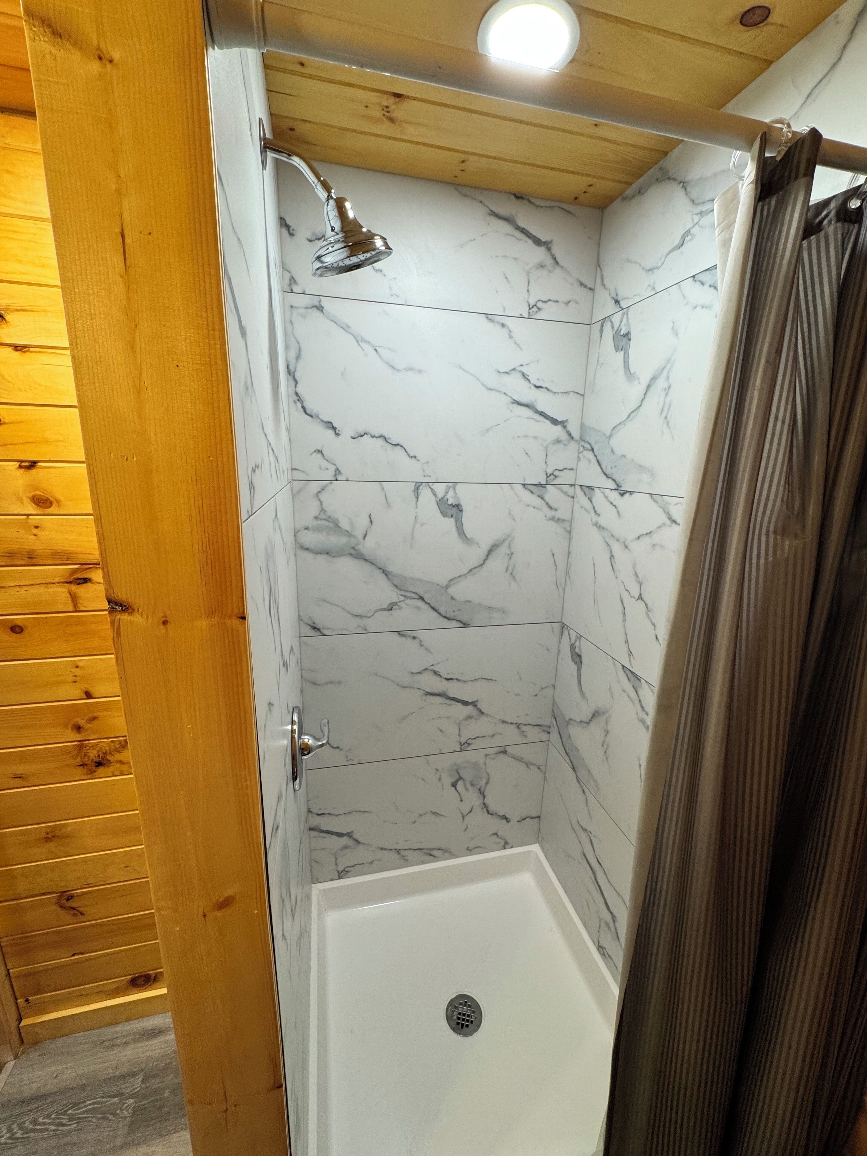 A shower with a marble wall and wooden ceiling.