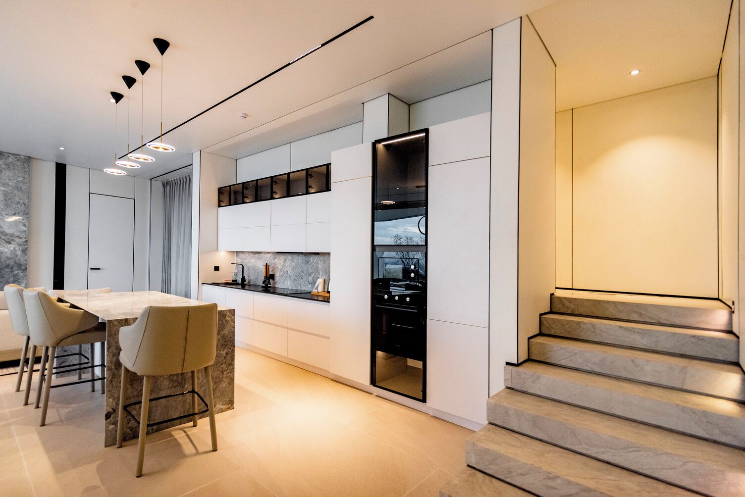 Una cocina moderna con electrodomésticos integrados, un comedor con mesa de mármol y una escalera con detalles de mármol.
