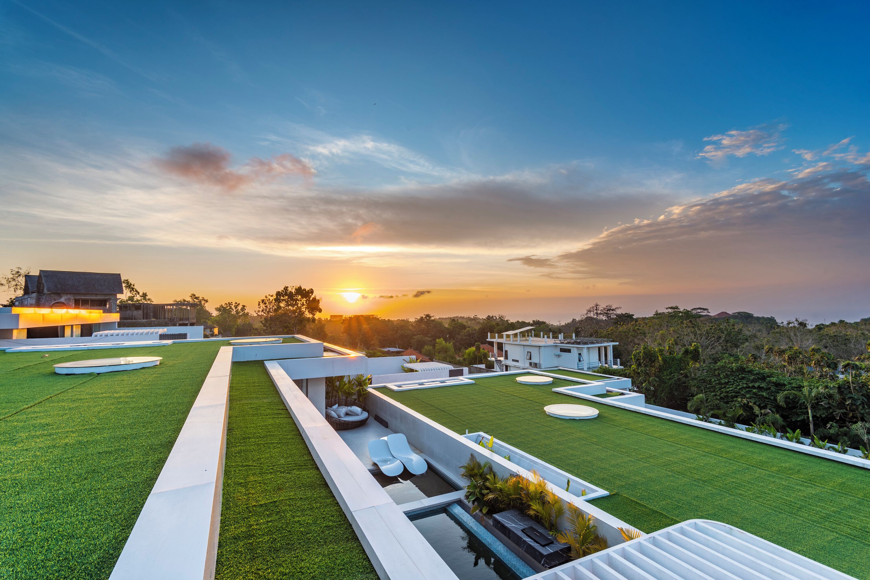 A rooftop terrace with a pool, seating areas, and a sunset view.