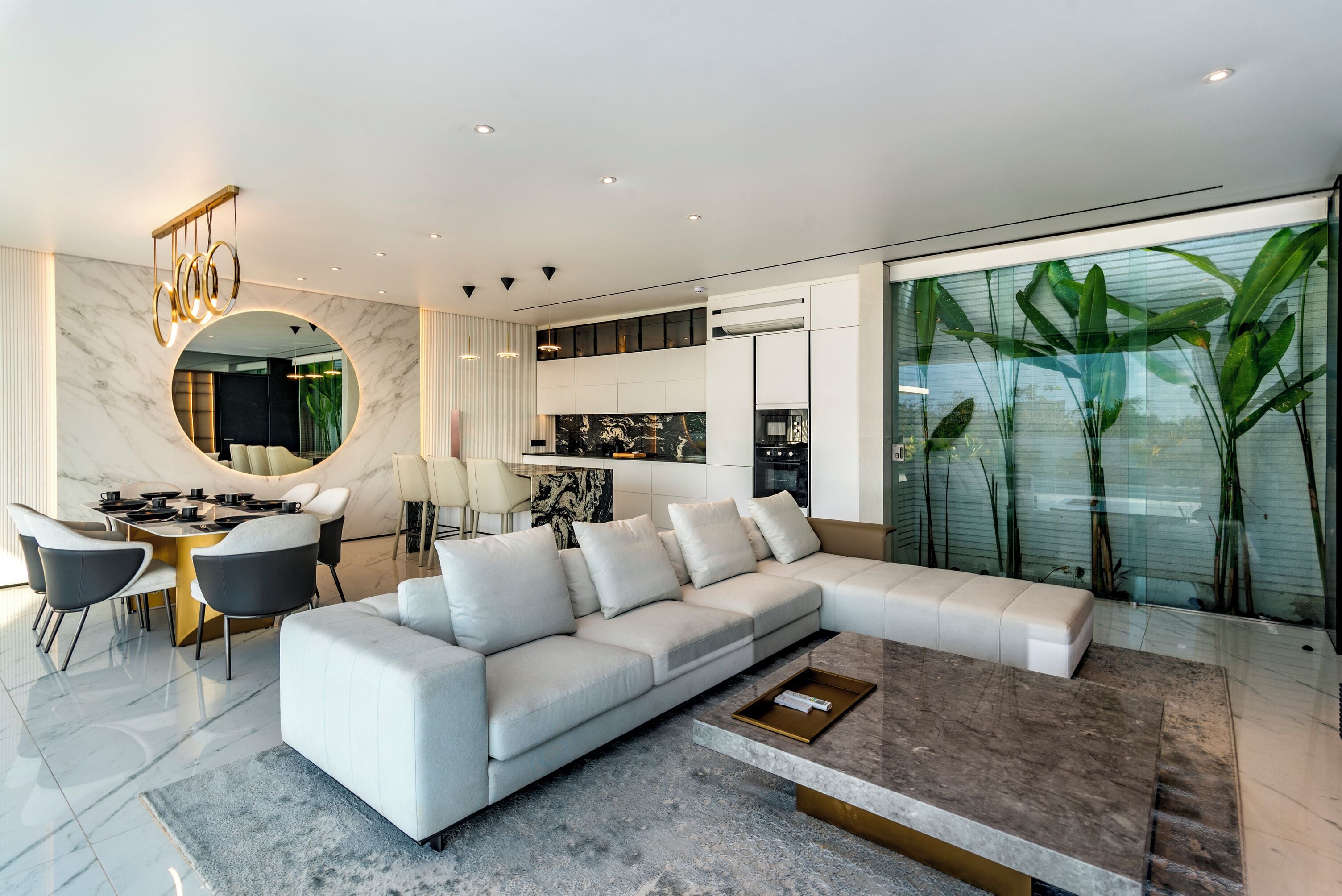 A modern living room with a white sectional sofa, a dining area with a round table, and a kitchen in the background.