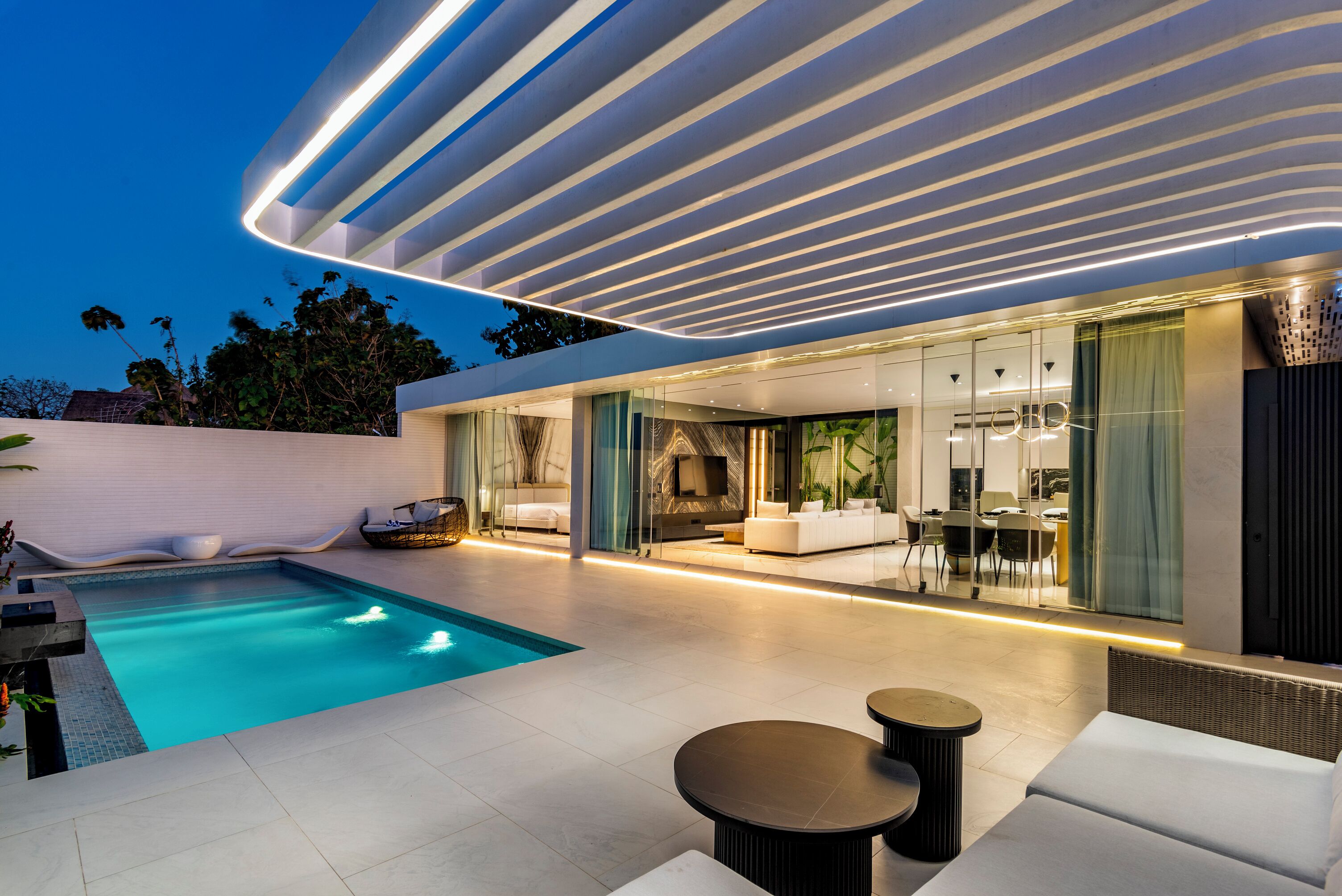 Un área de piscina moderna al aire libre con diseño contemporáneo, que incluye una piscina, zonas de estar y un porche cubierto.