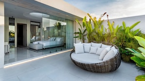 Una casa moderna con facciata in vetro, un divano in vimini circolare con cuscini e piante rigogliose.