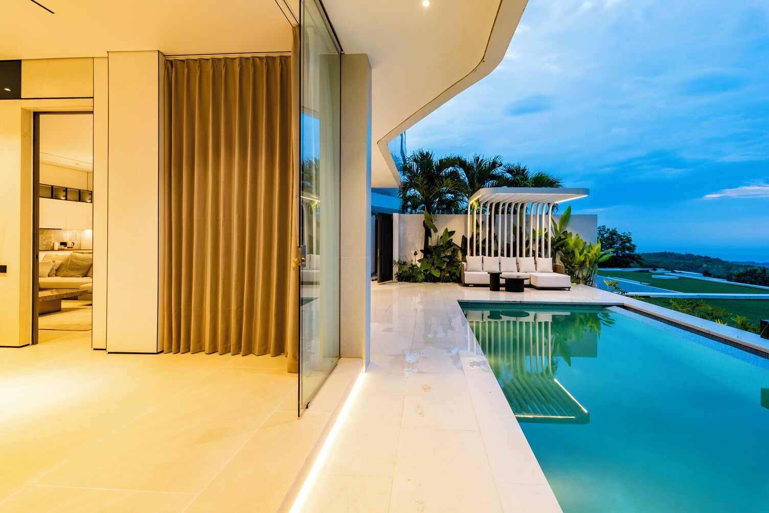 Un área moderna junto a la piscina, con puerta de cristal que da a un salón, una piscina y vistas del paisaje.