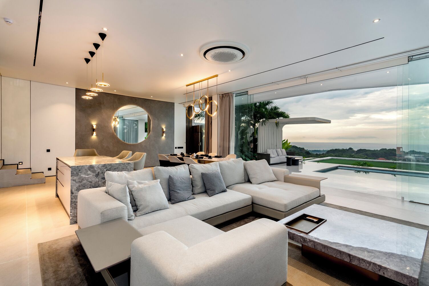 A modern living room with a large sectional sofa, a marble coffee table, and a dining area with a round table.