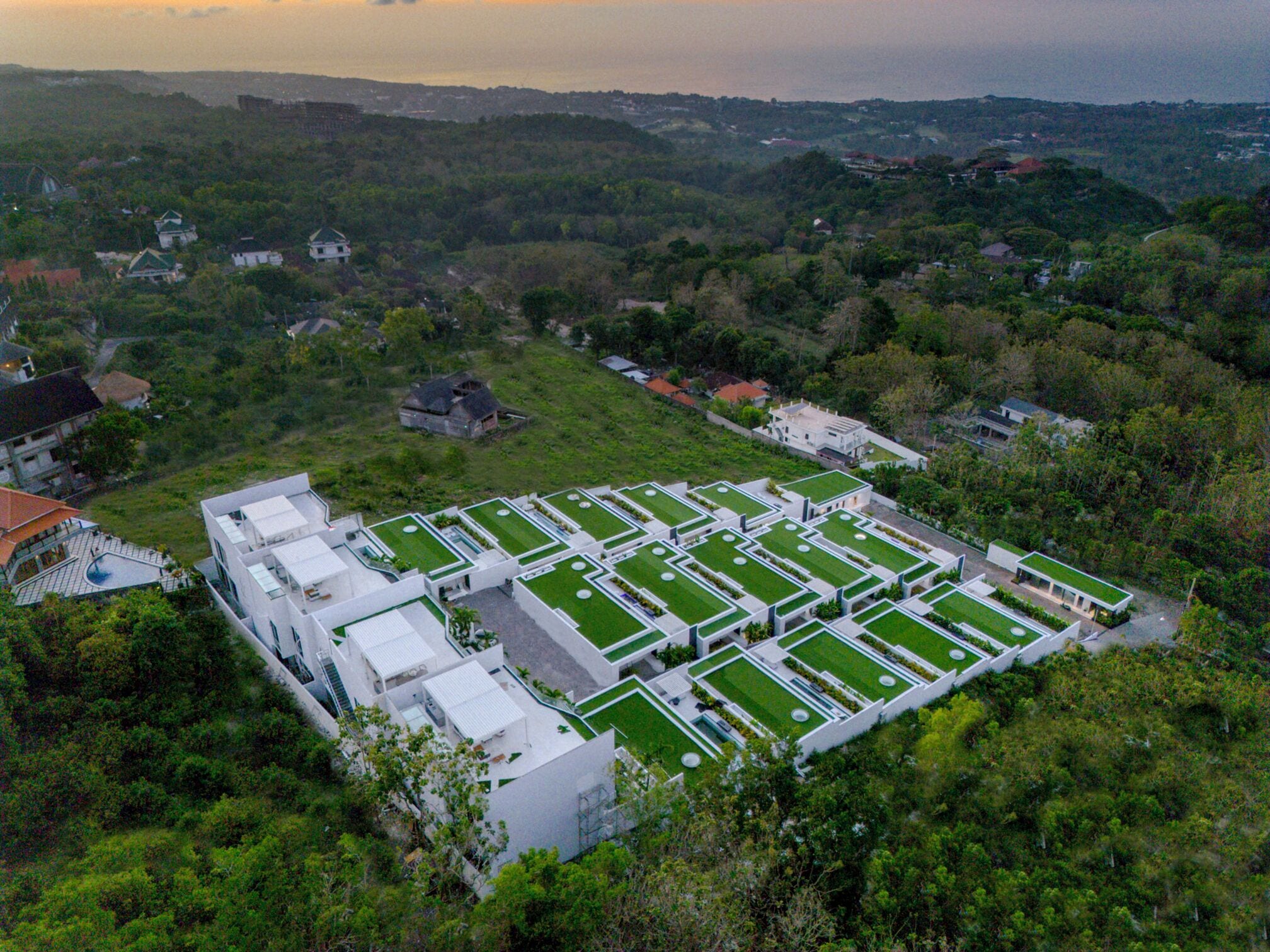 Vue aérienne d’un complexe immobilier moderne composé de plusieurs bâtiments dotés de toits végétalisés, entouré d’une végétation luxuriante et d’autres immeubles résidentiels en arrière-plan.