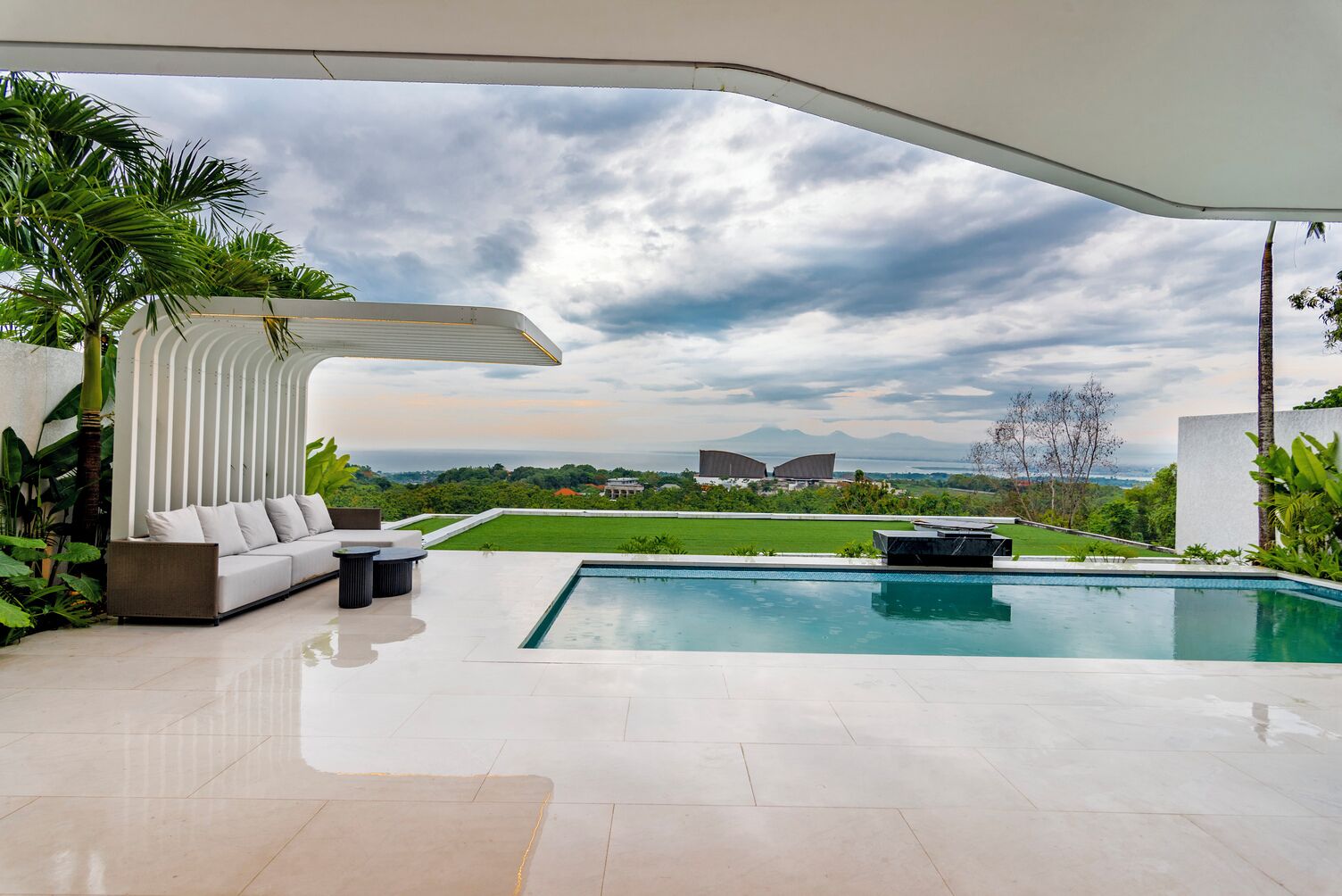 Zona de piscina exterior moderna amb un aulet blanc, un sofà i una taula de menjador.