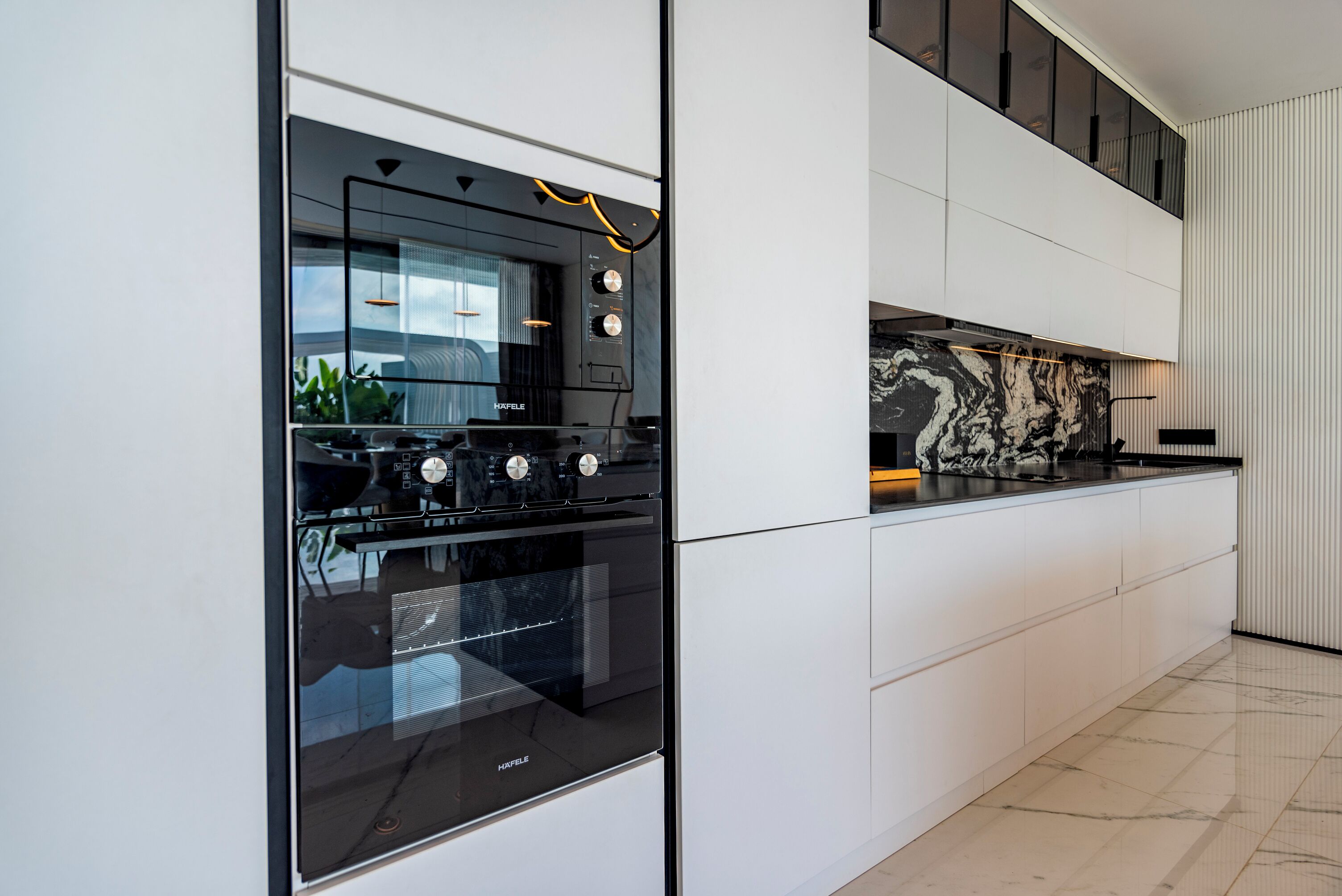 A modern kitchen with a built-in oven and a marble backsplash.